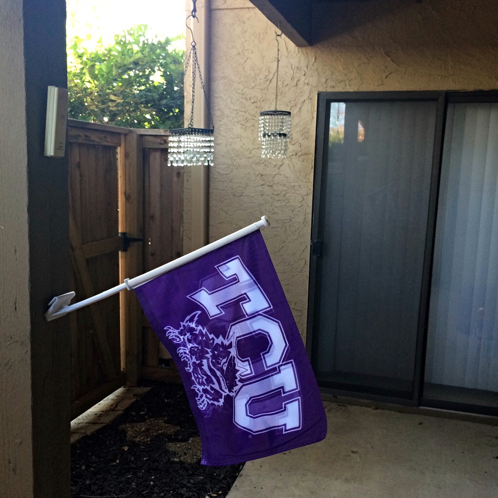 a purple TCU flag flies on a patio with hanging crystals, sliding door and wooden fence