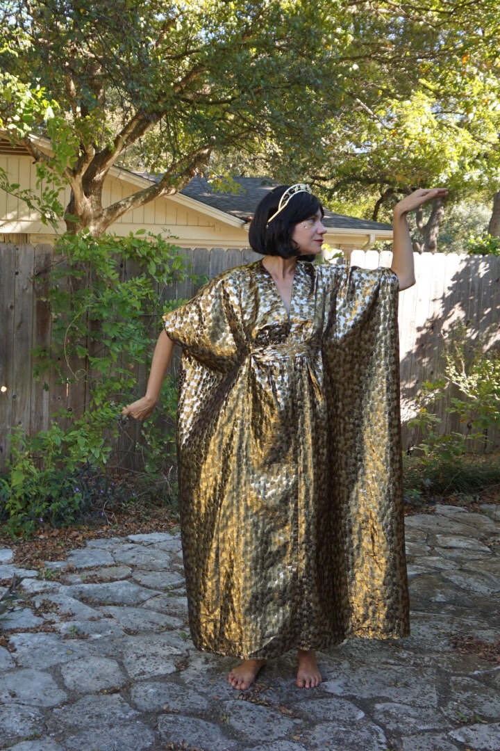 a woman in a gold caftan posing like Cleopatra