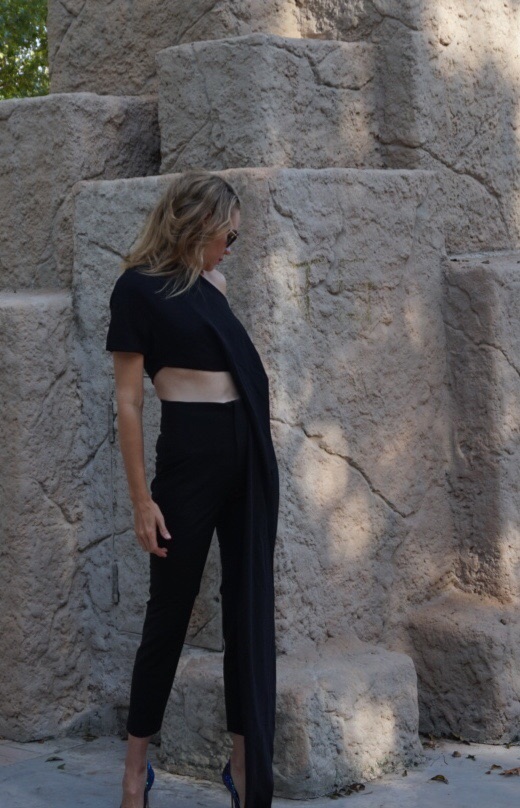 a blonde woman in a black crop top and black pants in front of stone