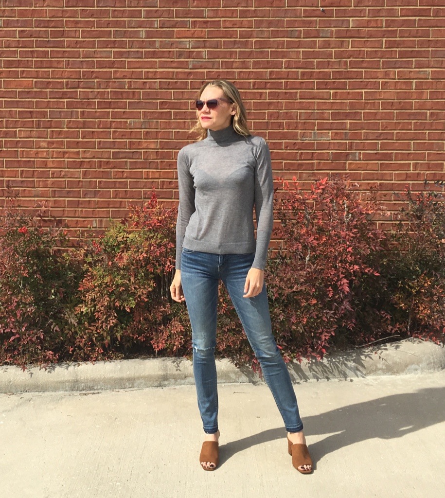 a woman in jeans and a grey turtleneck and brown sandals