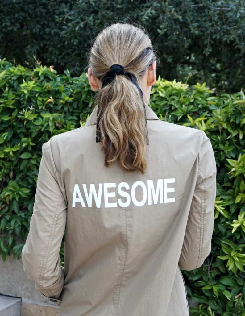 the back of a woman in a tan trench coat that reads AWESOME on it