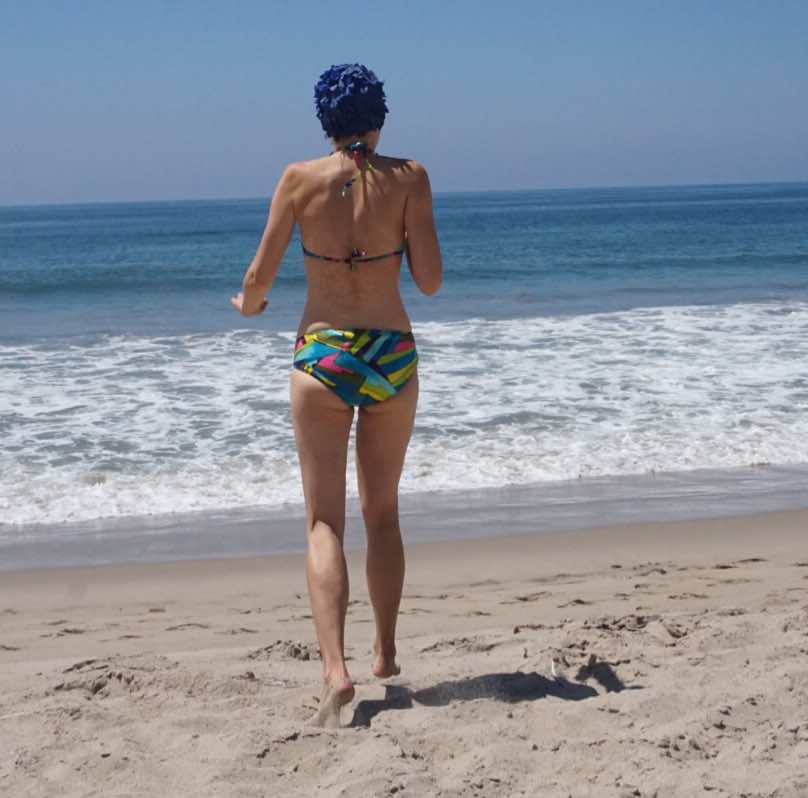 A woman in a vintage blue bikini and blue hair cap running into the ocean