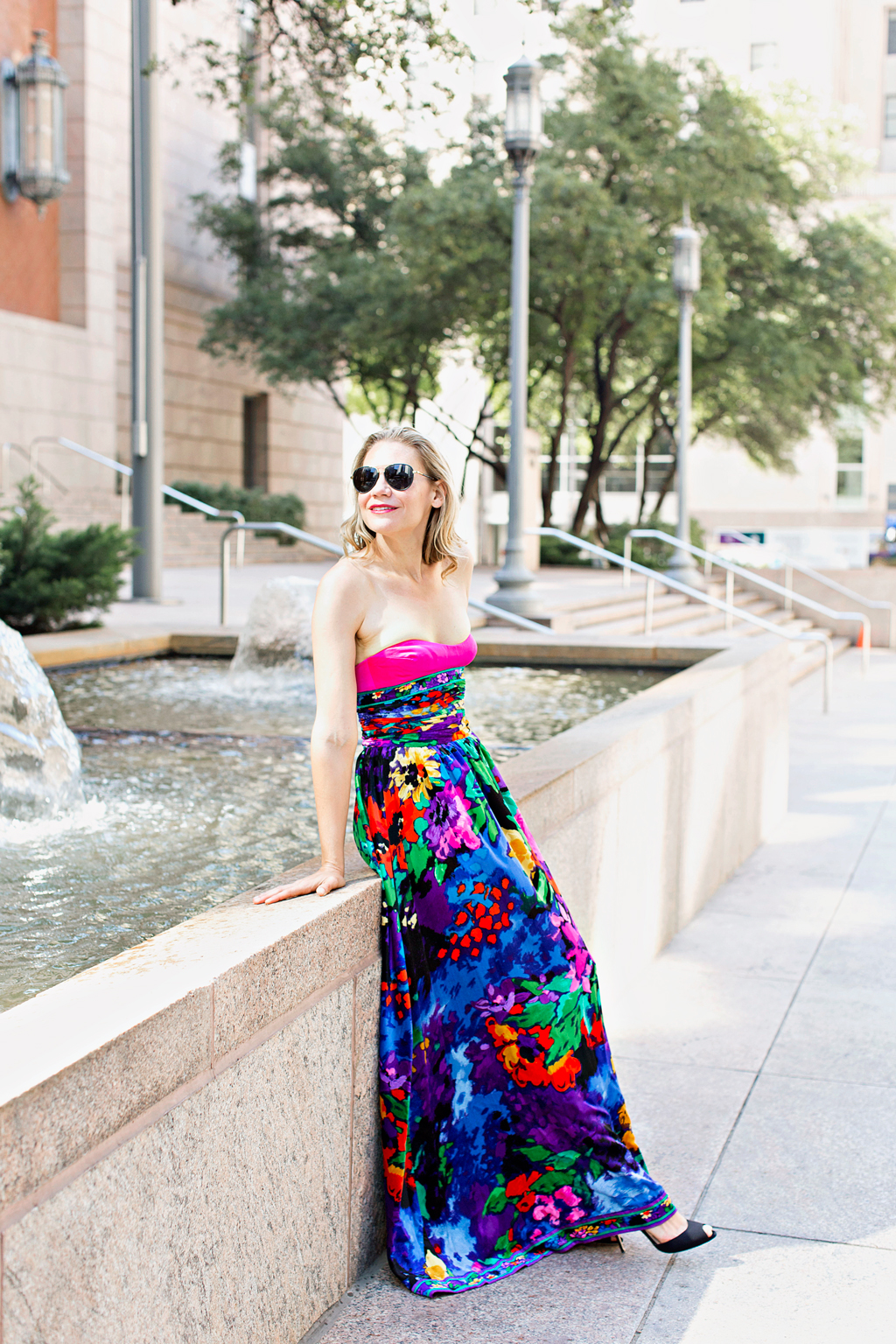 a pink silk and floral velvet gown in front of a fountain