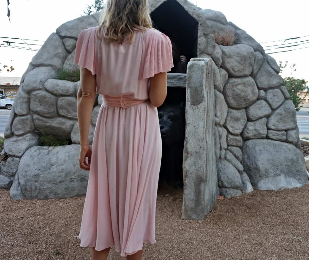 a woman in a pleated pink dress in front of a stone wall