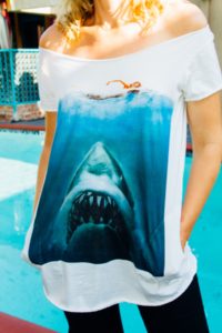 close up of a shirt with a shark coming up from the ocean with a woman swimming on the surface 