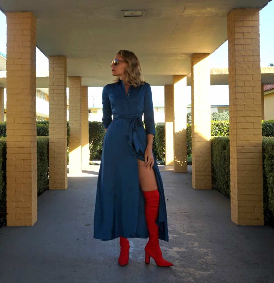 a woman in a blue satin shirt dress and red over the knee boots in a hallway