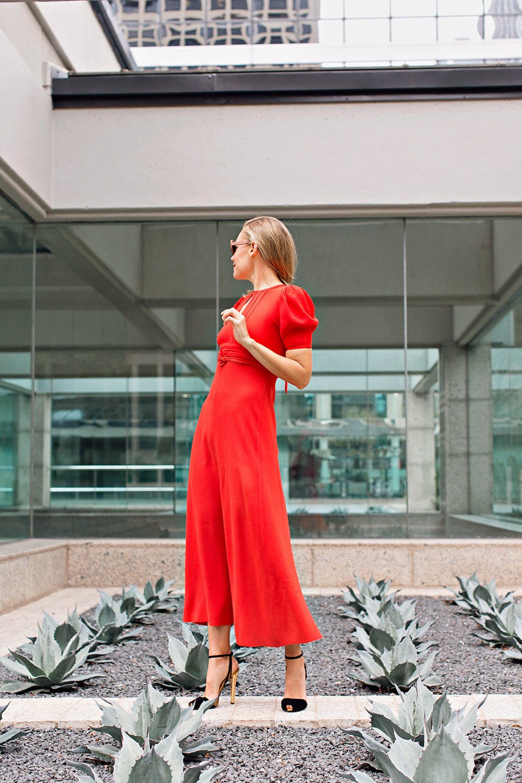a woman in a red short sleeve dress and black heels in a succulent garden 