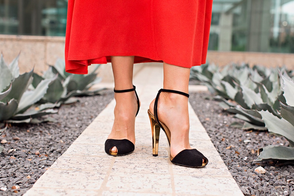 A close up of a red dress hem and black velvet and gold heels