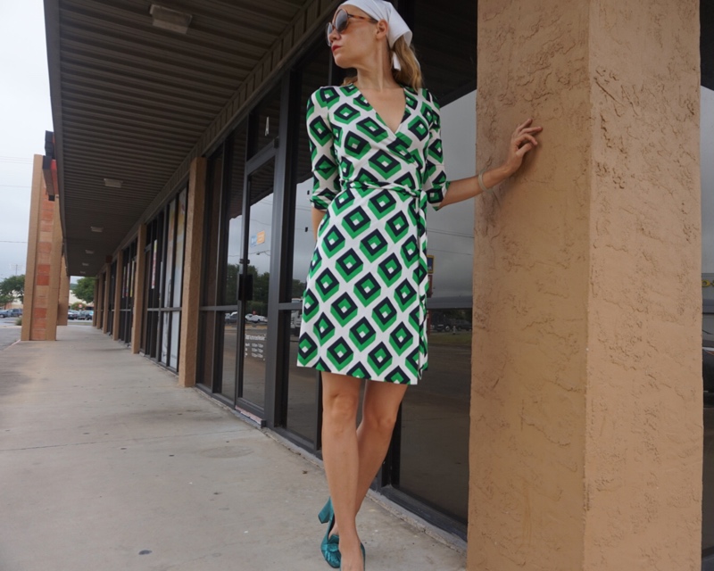 a woman in a green and white wrap dress, hair in a scarf and green loafers