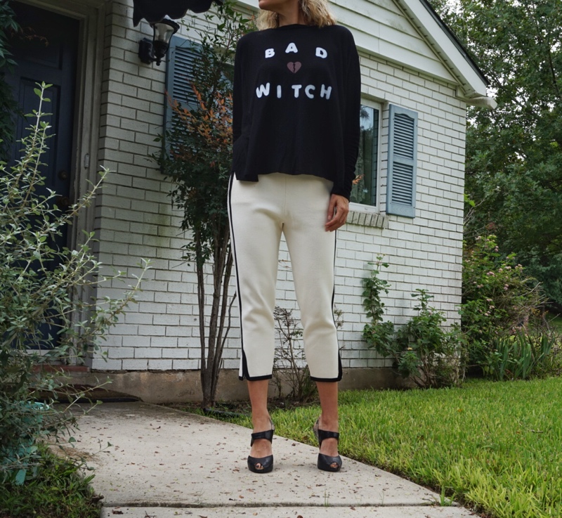a woman in a black shirt that says bad witch with white pants 