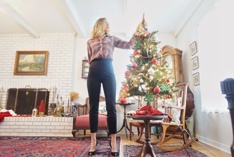 A woman in plaid shirt and black pants standing by a Christmas Tree