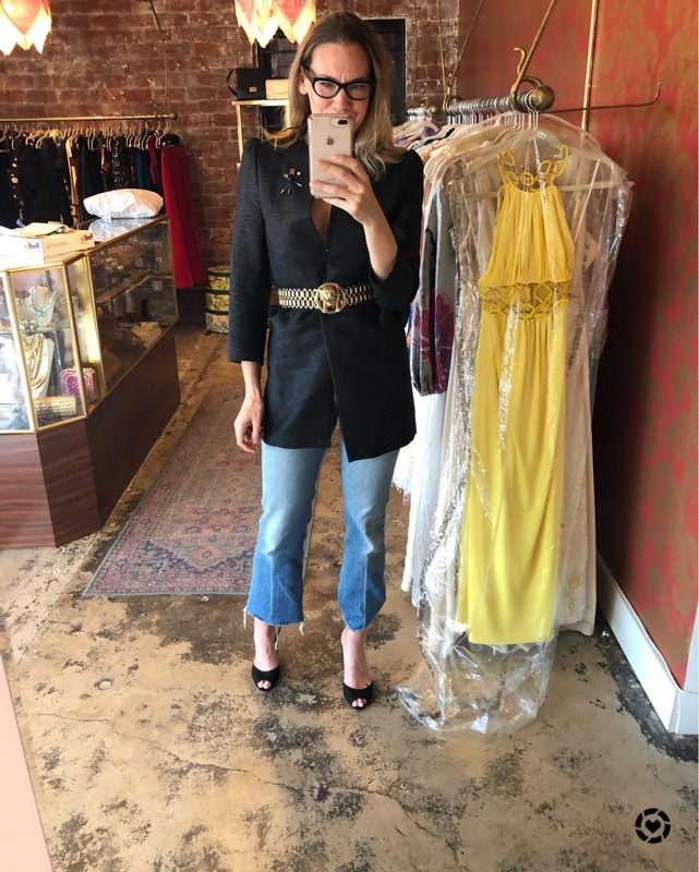 a woman with a black blazer belted with a gold lion belt, over jeans and wearing heels in a clothing store