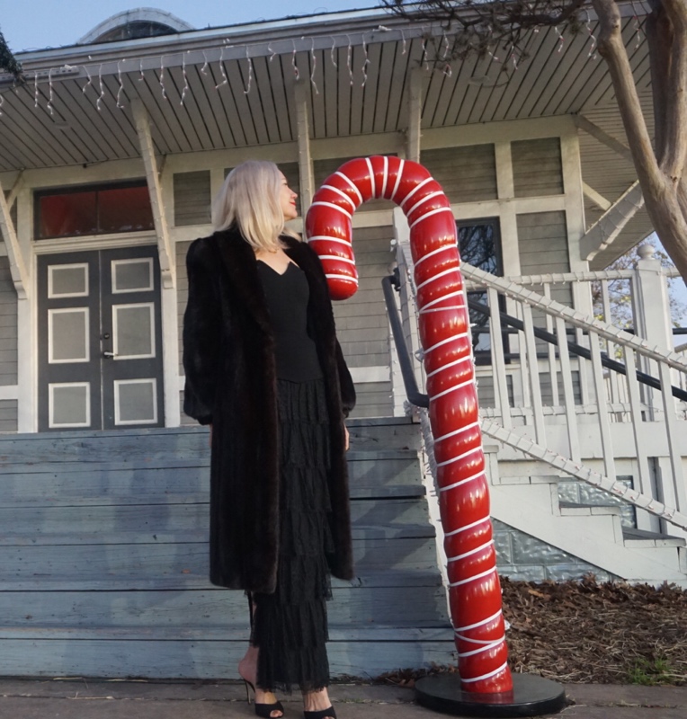 a blonde woman with a black skirt and coat by a red candy cane 