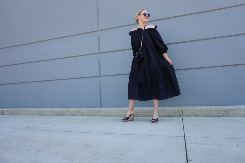 A woman in an off the shoulder black midi dress and wedges 