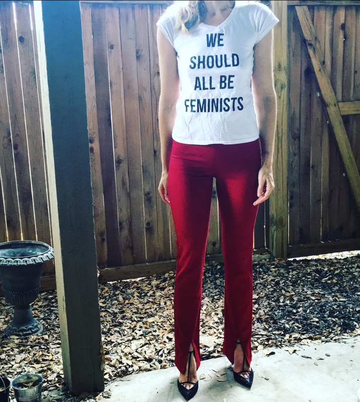 a woman in a white tee with black letters saying we should all be feminists and red pants and black heels 