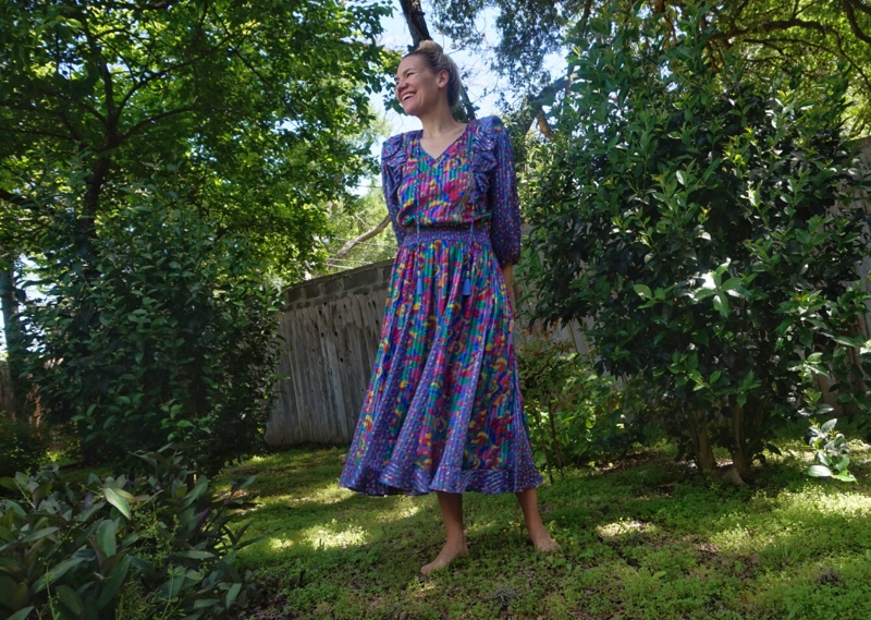 a woman in blue and yellow floral dress standing in a green yeard