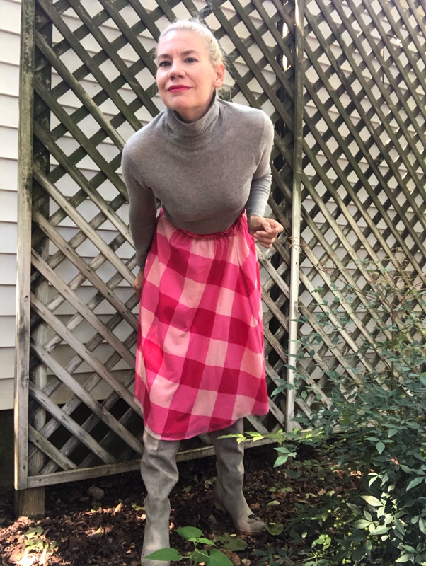 a woman in a grey sweater and boots and a pink checked skirt