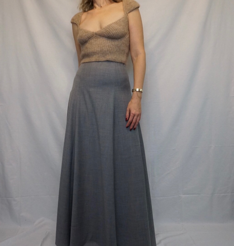 Close up of a woman in a tan sweetheart neckline sweater and grey maxi skirt in front of a white background 
