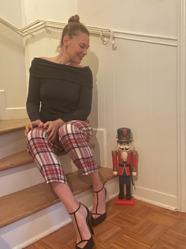 a woman in plaid pants and a grey sweater sits on stairs next to a nutcracker 