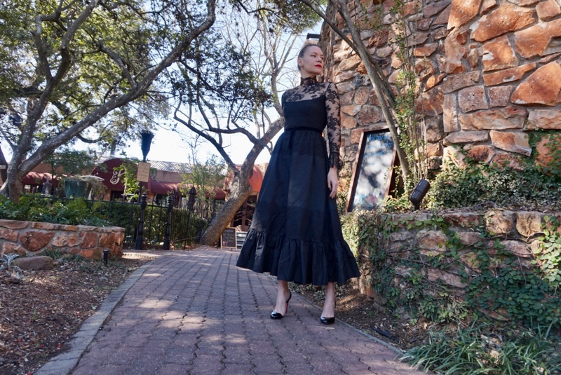 a woman in a black lace dress on a stone walk with a stone wall and trees