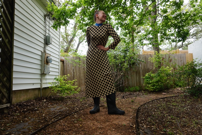 a woman in a checked dress and rain boots in a green garden