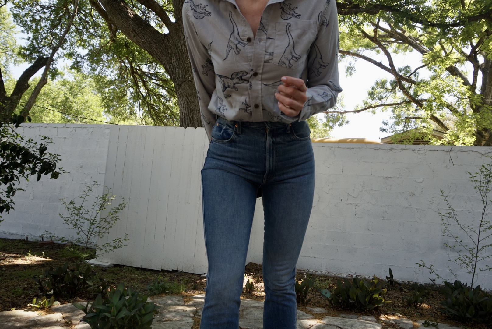 A close up of a woman in a dino printed button down and jeans in front of a white fence