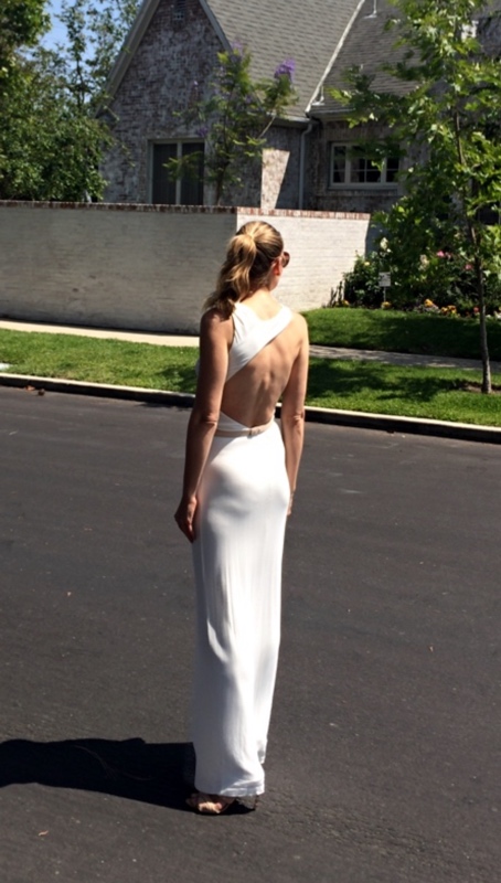 the back of a woman in a white dress with the back cut out in front of a house