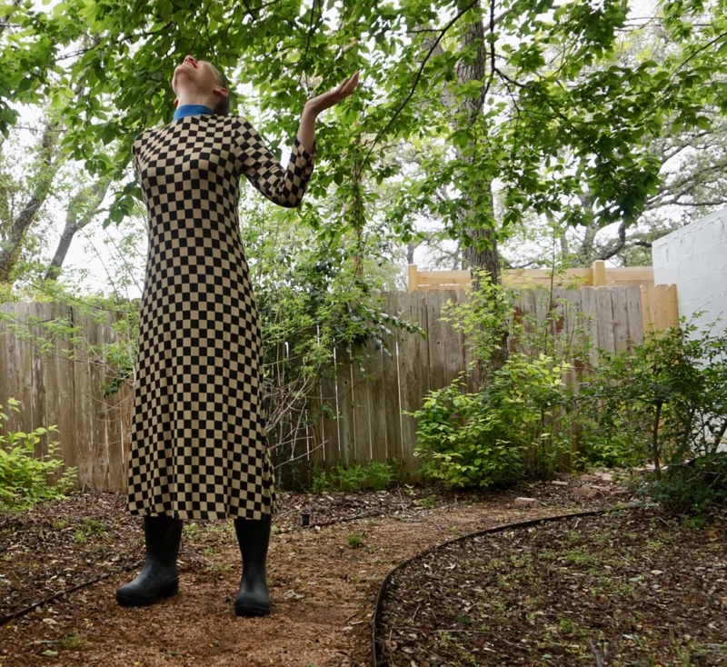 woman in a checked dress and rain boots looks for rain in a green garden