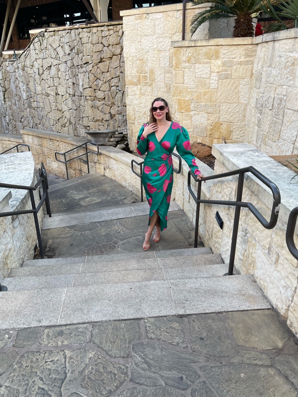 a woman in a green silk wrap dress with pink roses stands on a stone staircase