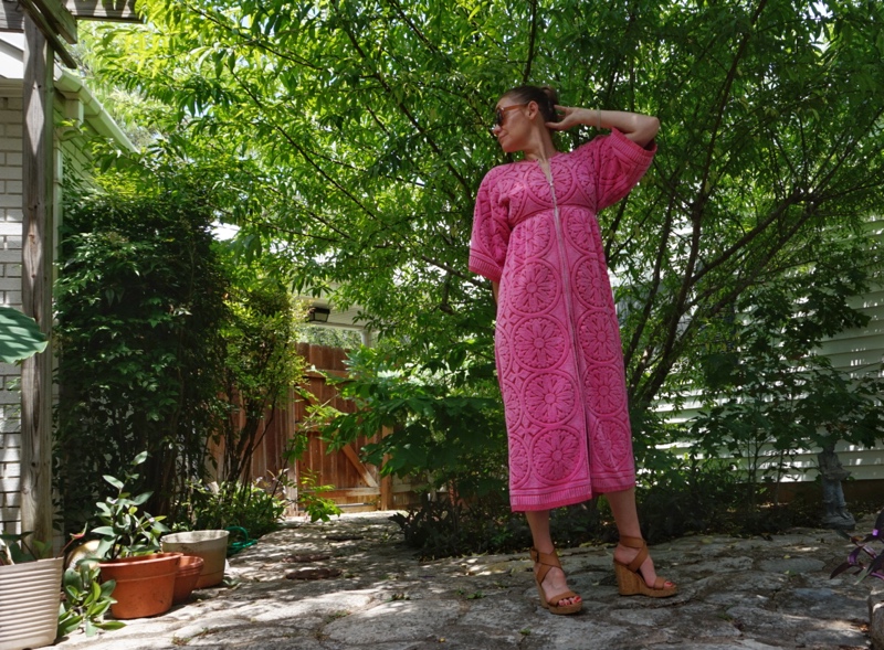 a woman in a pink robe made from towels stands in front of green trees