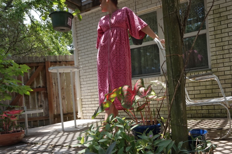 a woman in a pink robe made of towels in front of hanging plants and a white wall