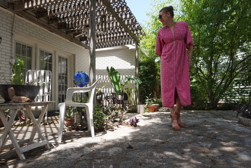 a woman in a pink dress that's made out of towels in front of green trees and patio furniture