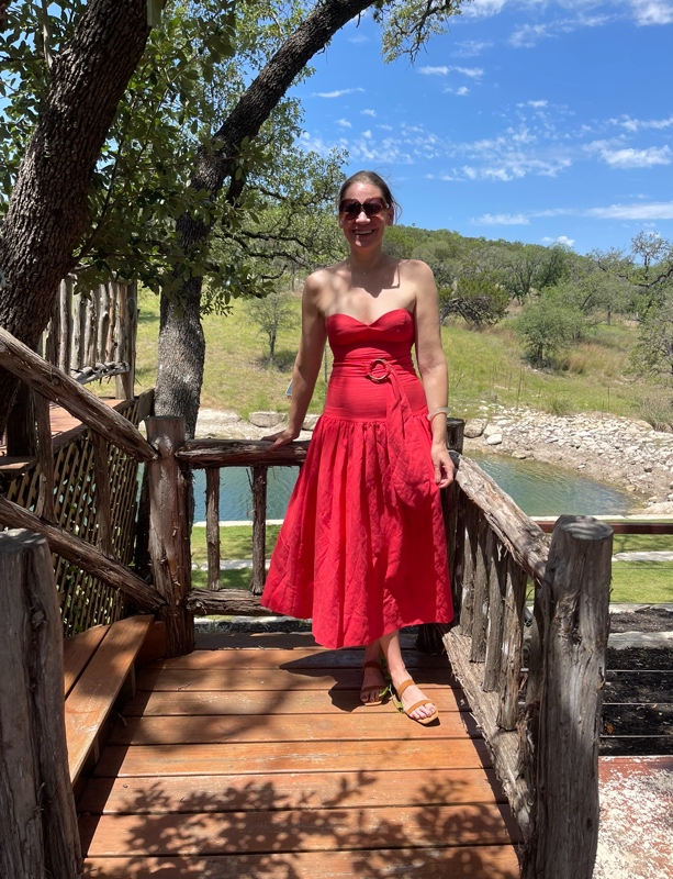 a woman in a strapless orange dress on a deck in front of river