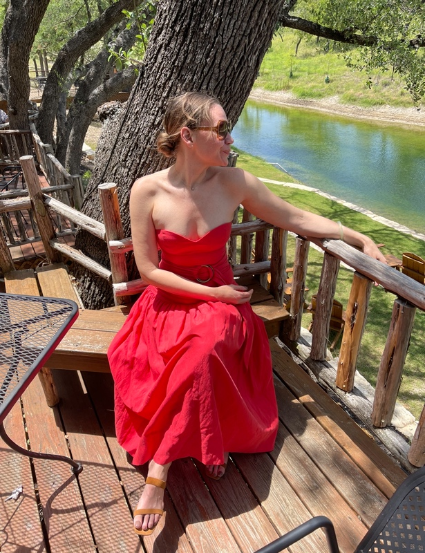 a woman in a strapless orange dress in front on a deck in front of a river