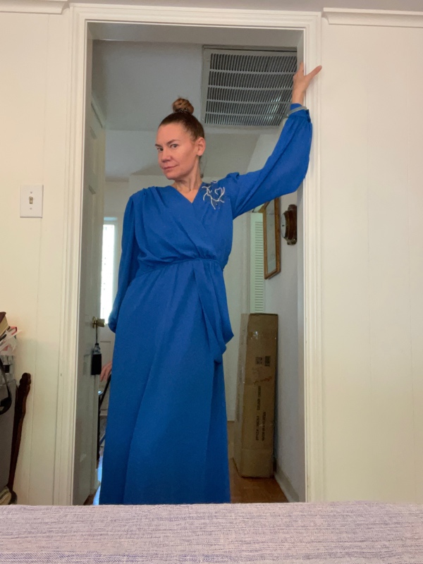 a woman in a blue dress leans against a door frame
