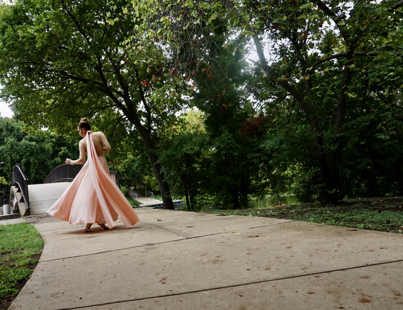 a woman in a peachy pink halter dress twirls in the park