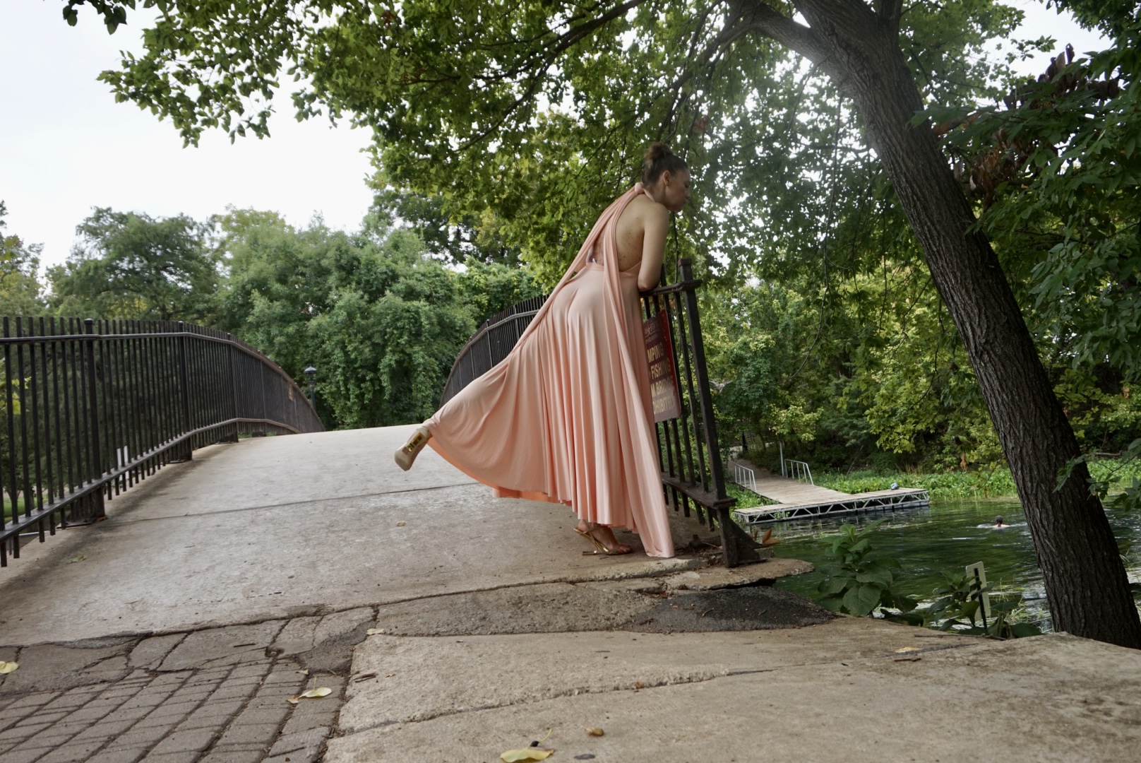 a woman in a peachy pink  halter dress twirls in a park