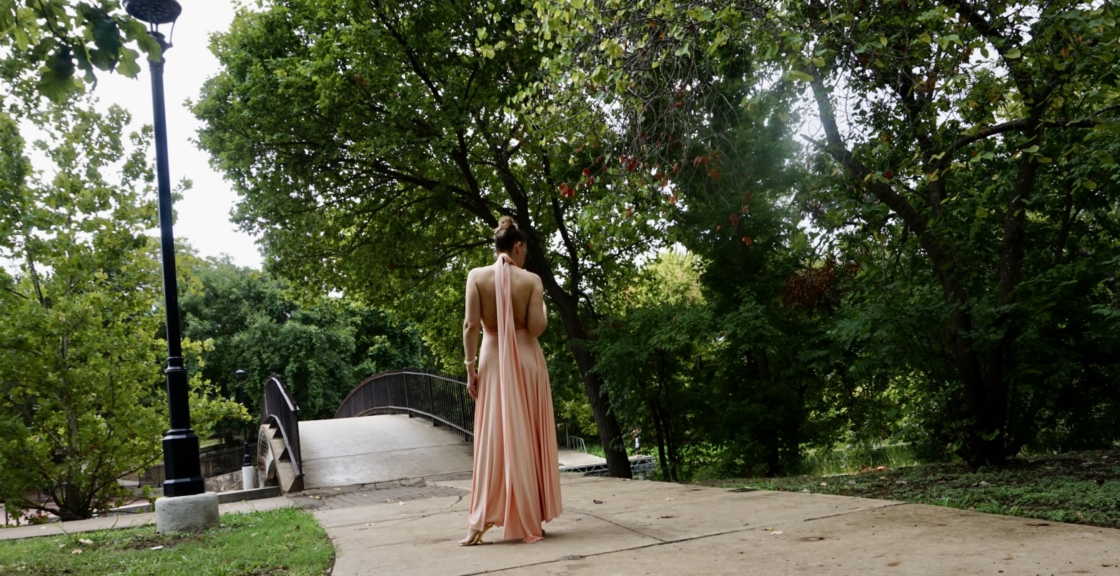 a woman in a peachy pink halter dress twirls in a park