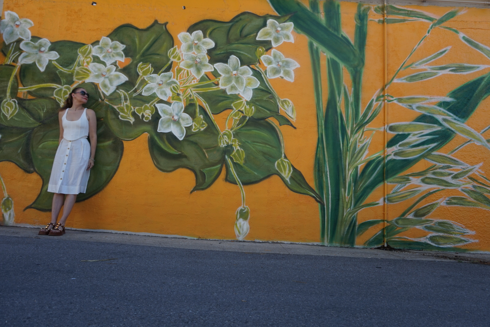 a woman in a white skirt and top in front of a yellow wall with flowers painted on it