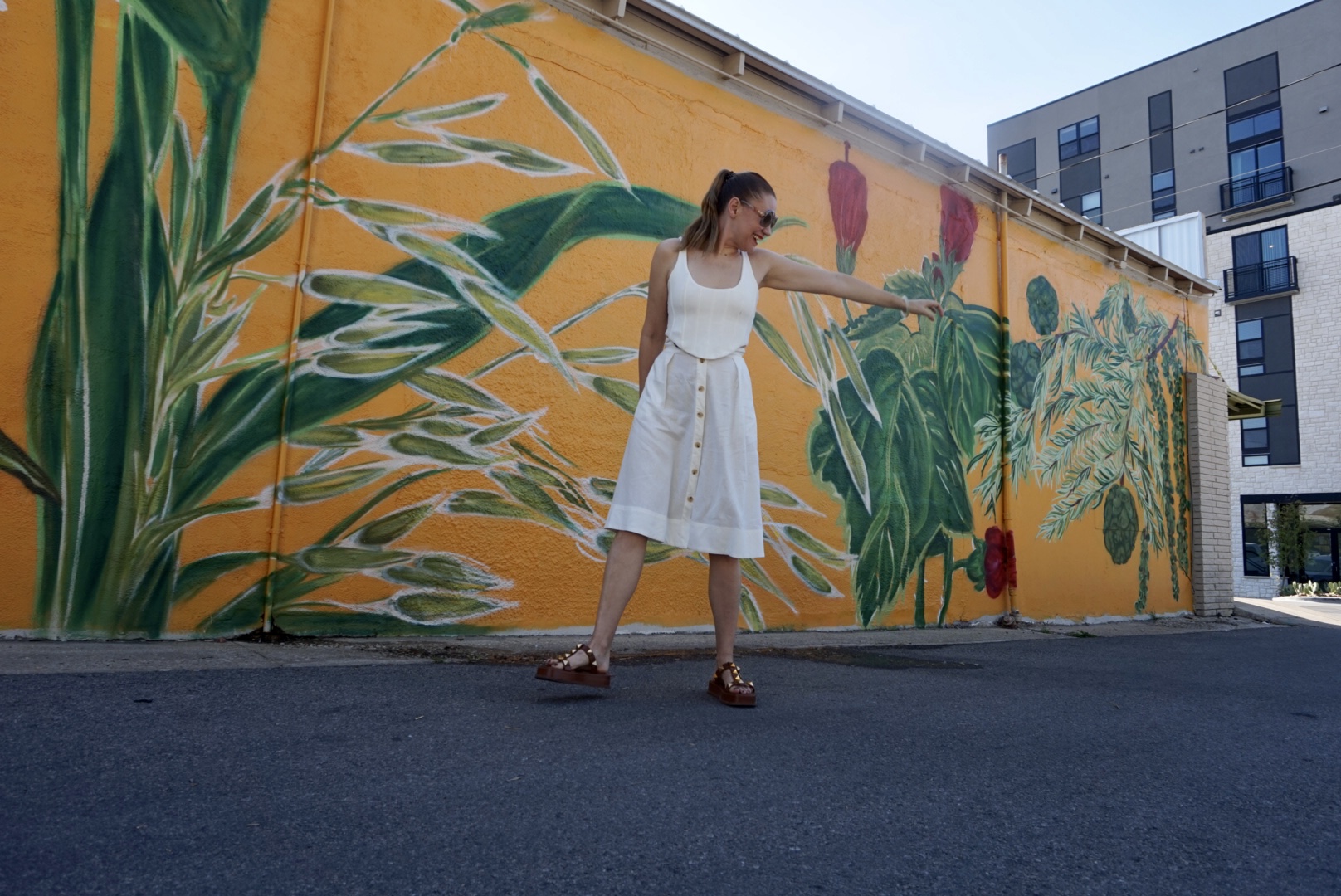 a woman with a white skirt and top in front of a yellow wall with flowers painted on it