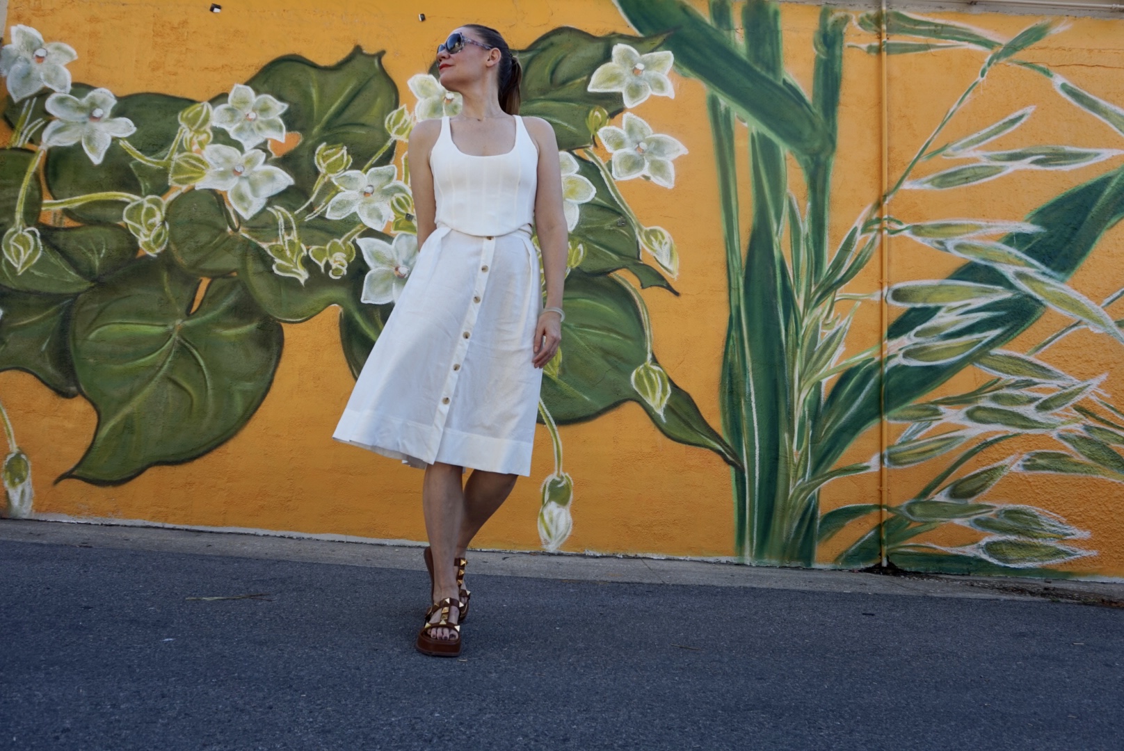 a woman wearing a white skirt and top in front of a yellow wall with painted flowers