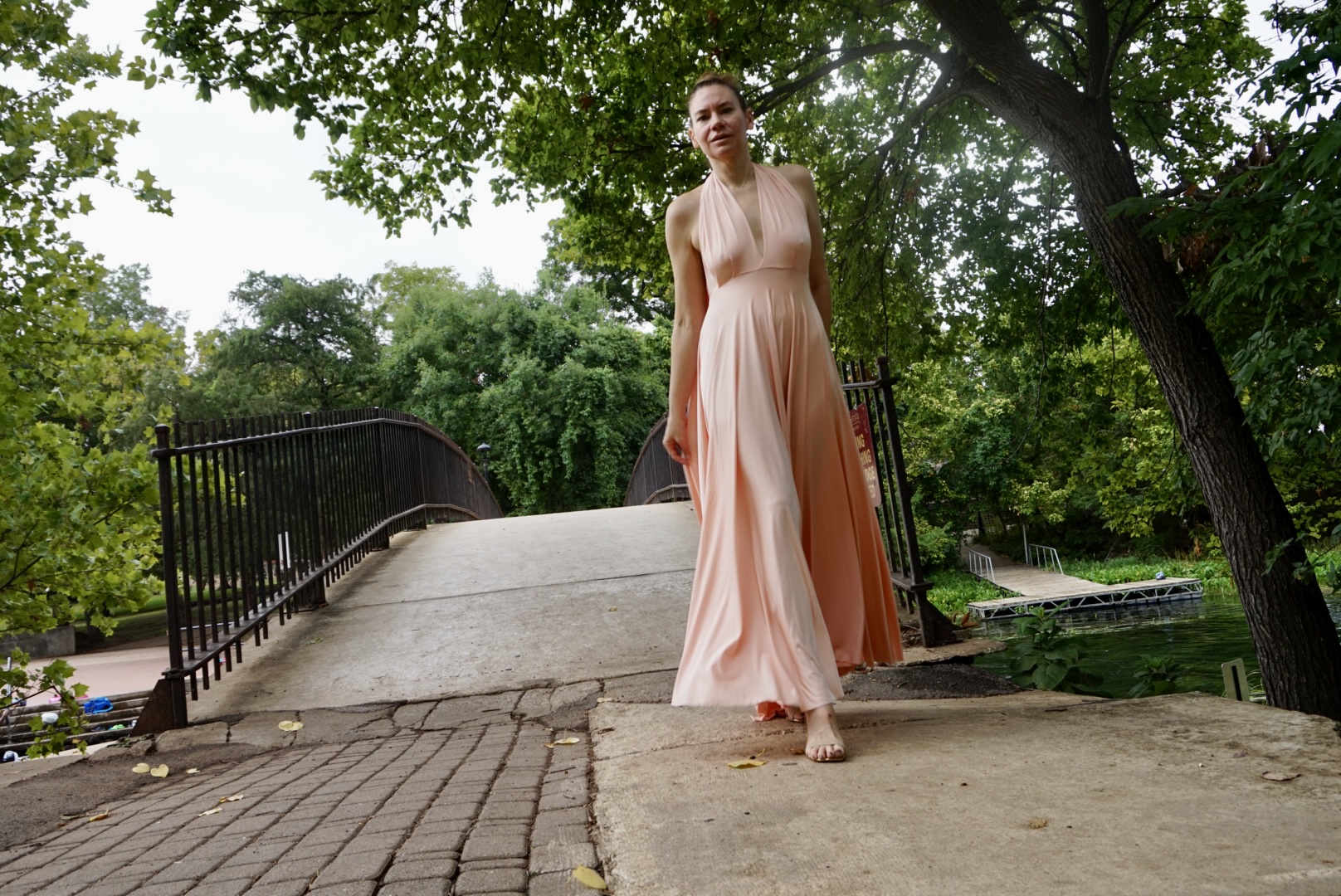 a woman in a peachy pink halter dress twirls in a park