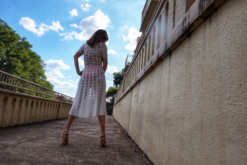 a woman in a white crochet dress stands with her back to the camera