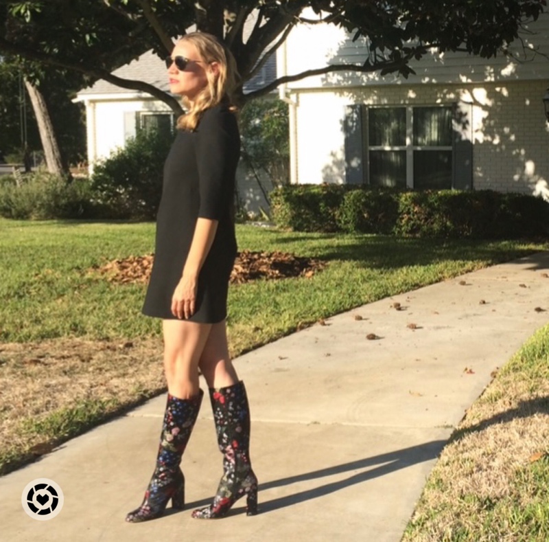 a woman in floral boots and a black mini dress in front of green trees and a white house