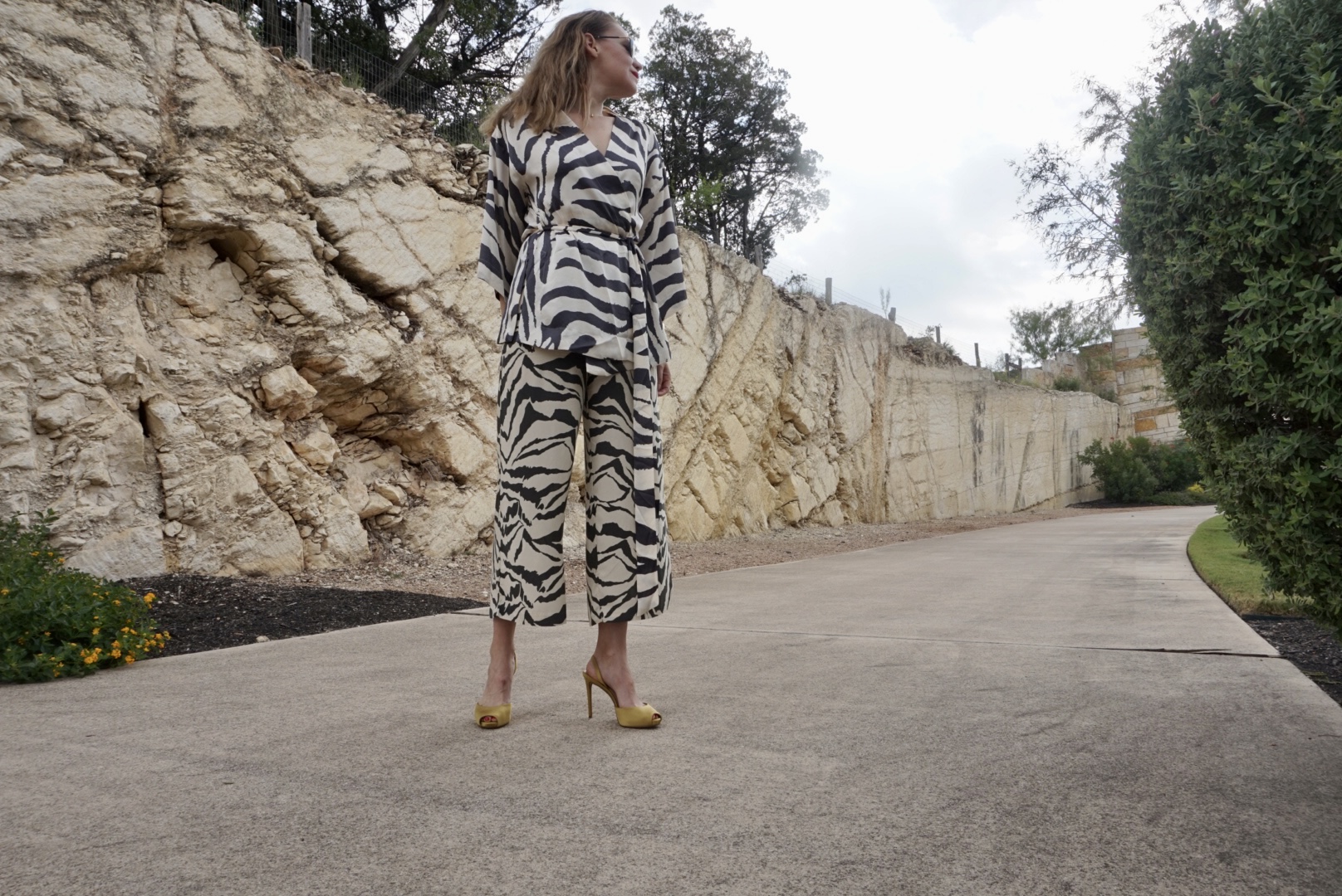 a woman in a zebra print suit and yellow heels in front of a stone wall