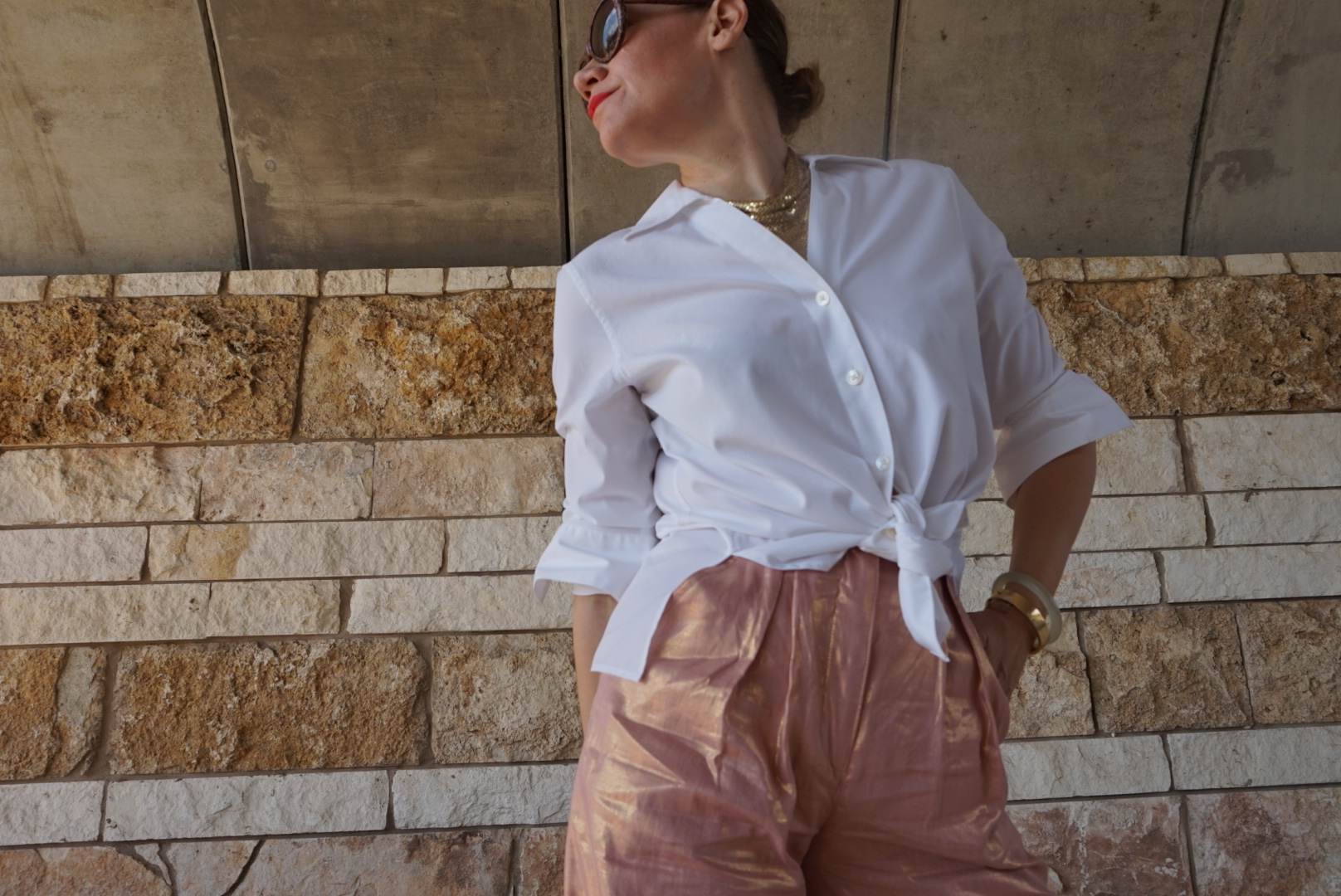 a woman in a white button down and rose gold pants under a bridge