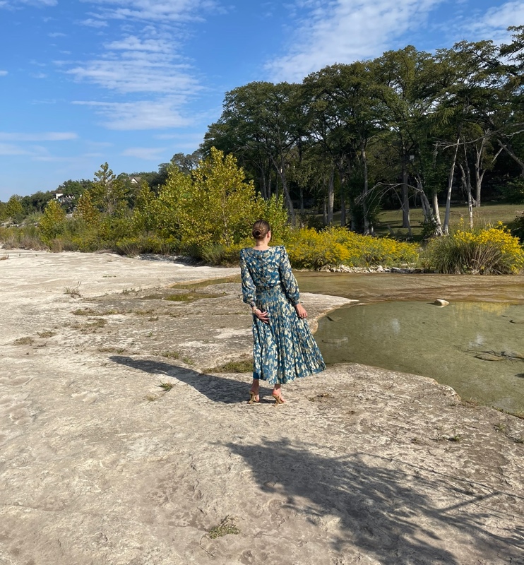 a woman in a teal and gold lame dress on rocks by a lake