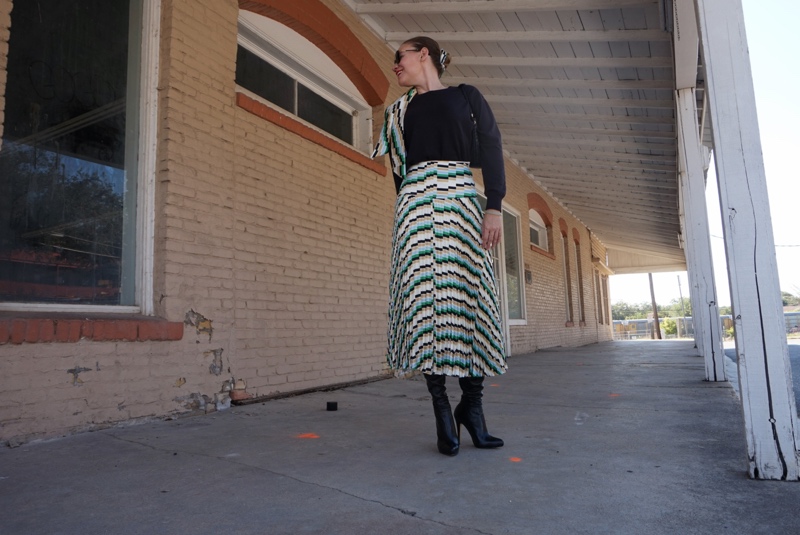 a woman in a pleated print skirt and black sweater on a sidewalk