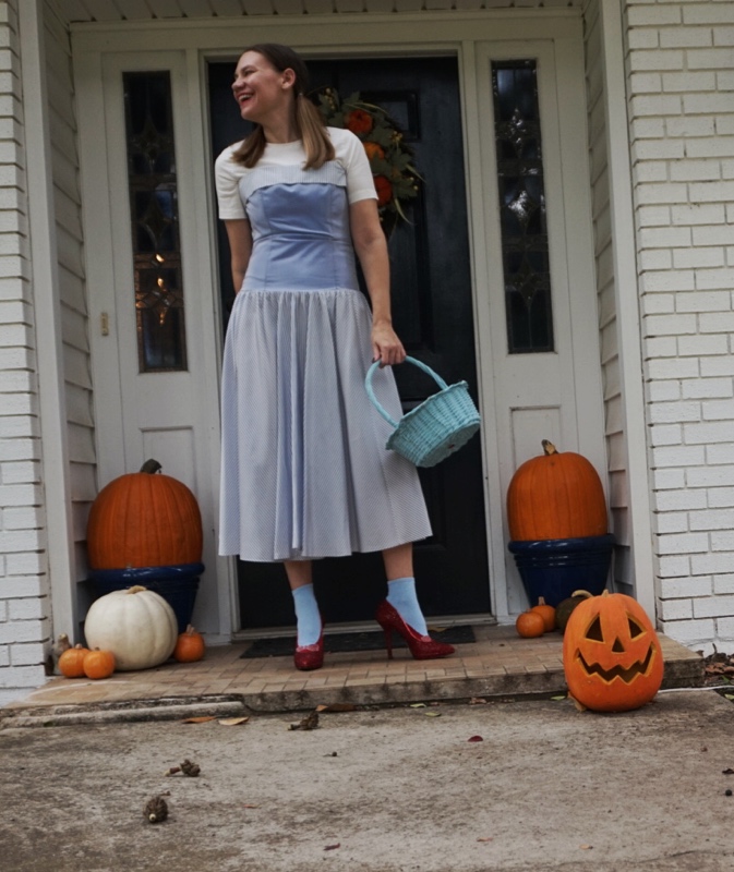 a woman with pumpkin in pigtails, red ruby shoes, a blue striped dress, white undershirt 