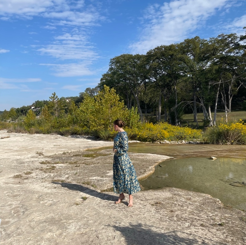 a woman in a gold and teal lame dress on rocks by a lake